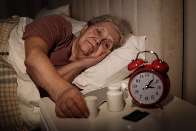 Photo of Elderly woman suffering from insomnia taking pill bottle in bed at night