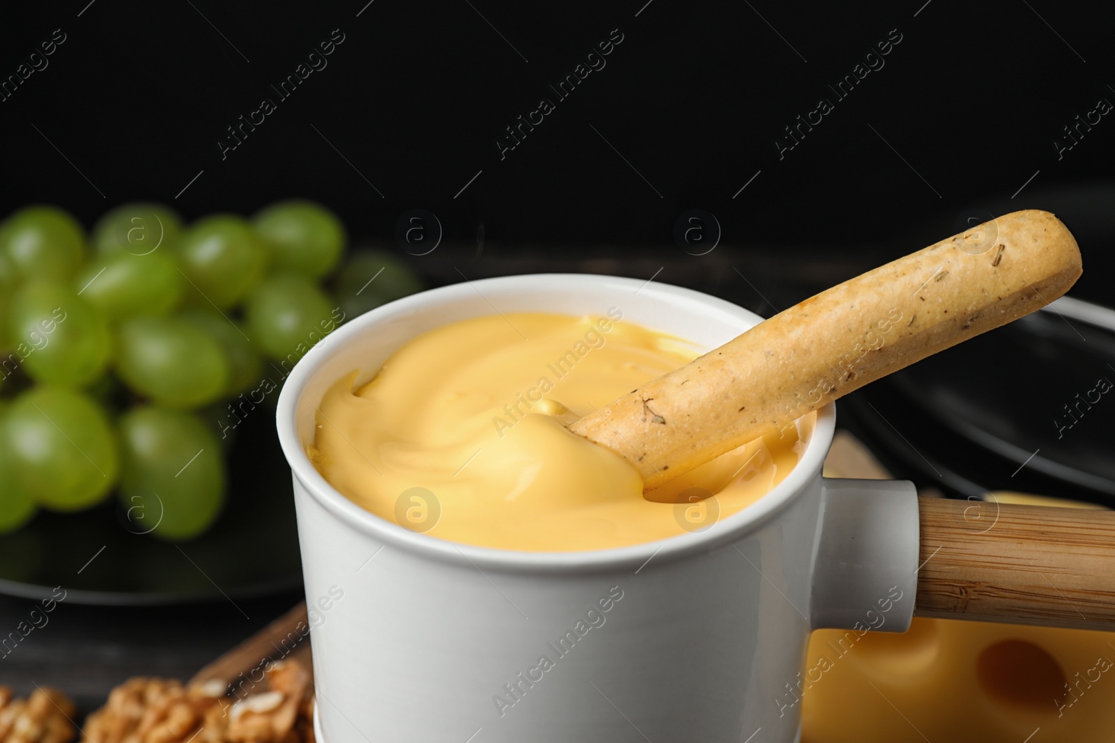 Photo of Pot of tasty cheese fondue and bread stick on black background