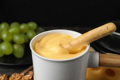 Pot of tasty cheese fondue and bread stick on black background