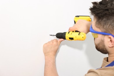 Photo of Young worker in uniform using electric drill indoors. Space for text