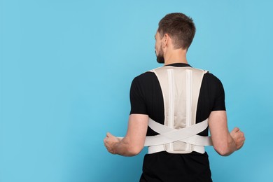 Man with orthopedic corset on blue background, back view. Space for text