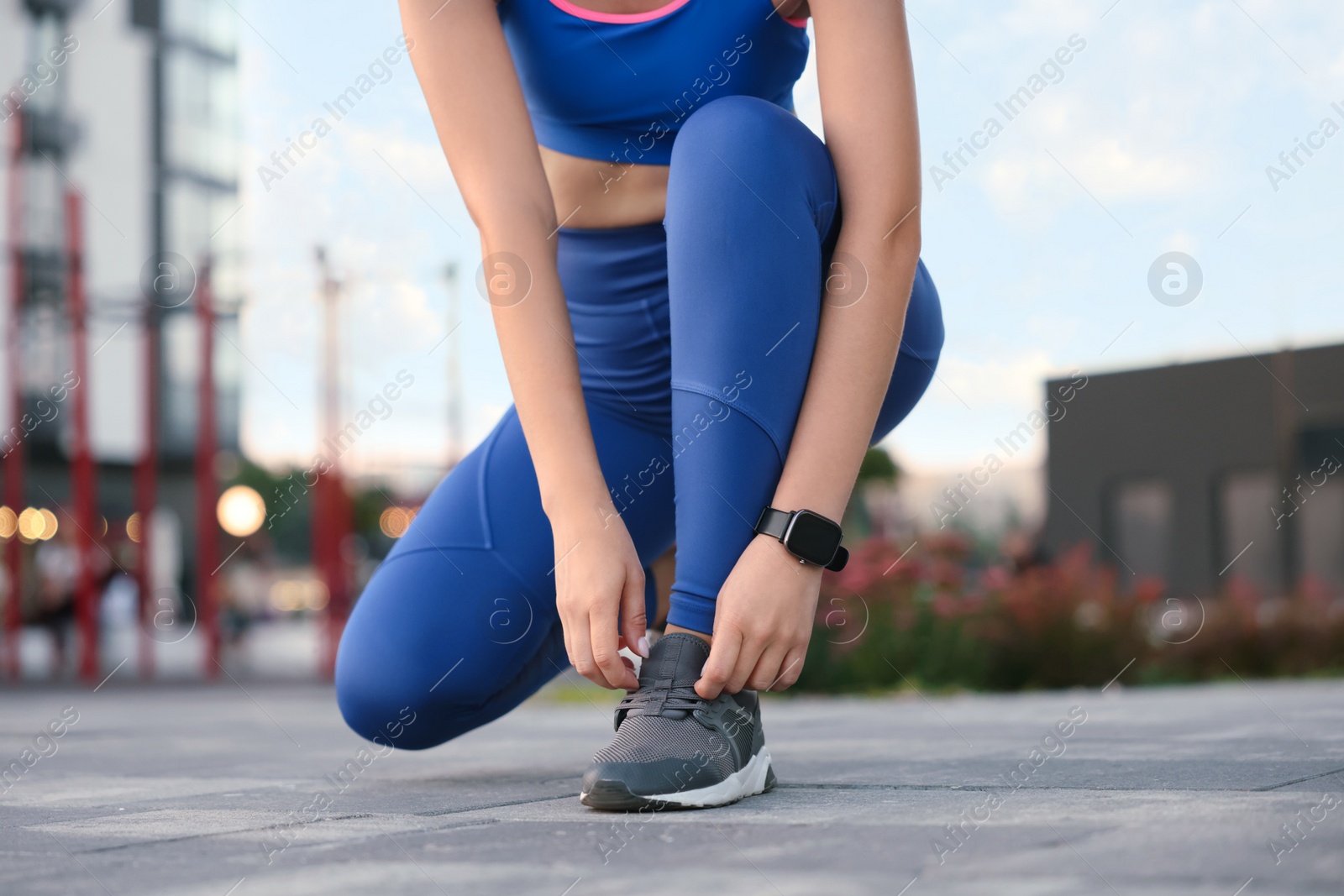 Photo of Woman in stylish sportswear tying shoelace outdoors, closeup