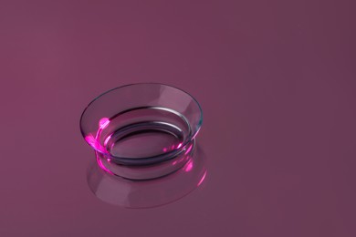 Photo of One contact lens on pink reflective surface. Space for text