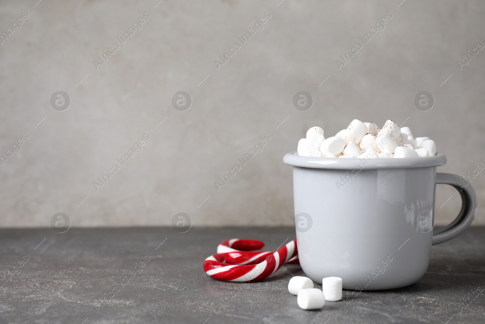 Photo of Cup of tasty hot drink with marshmallows near candy canes on grey table. Space for text