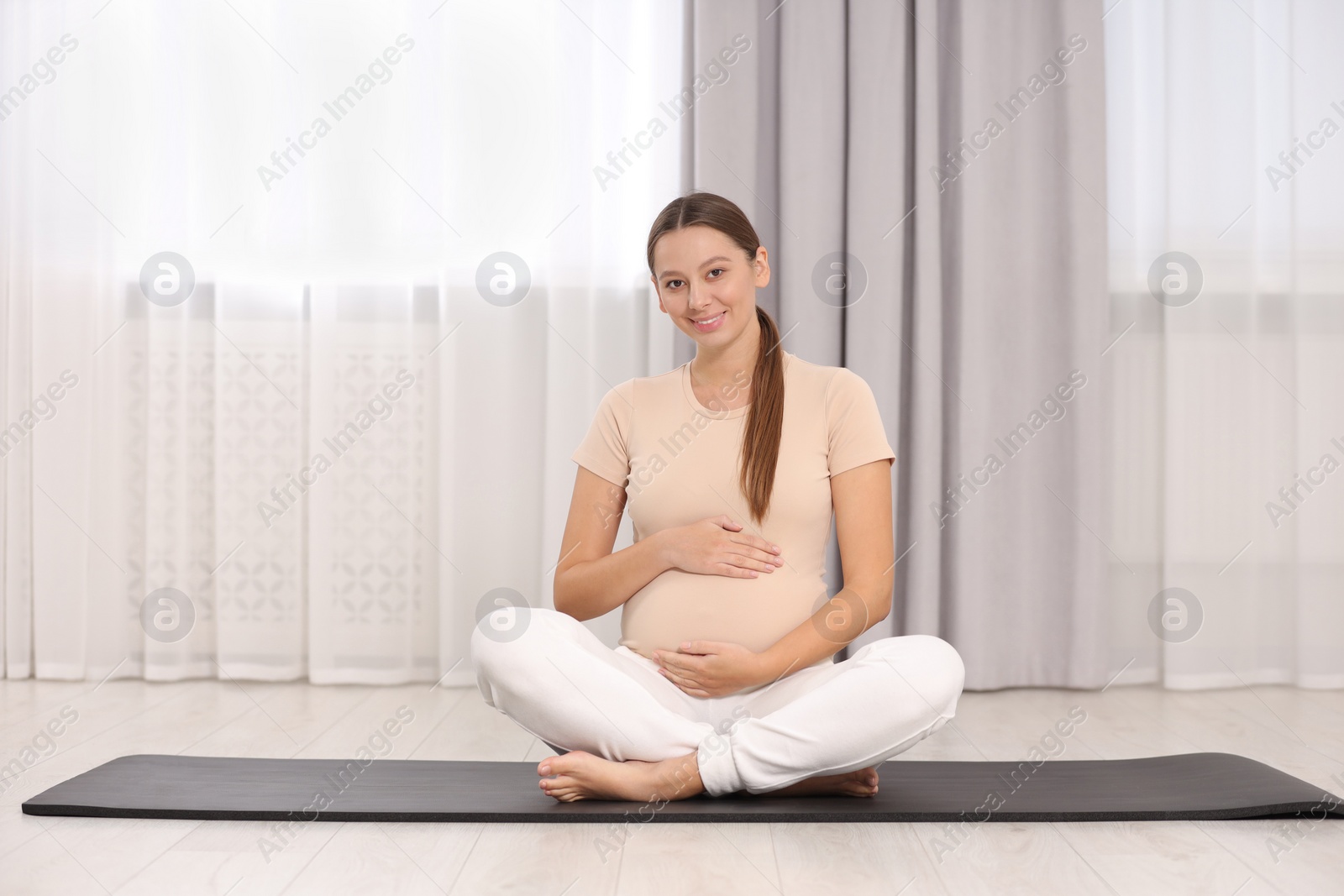 Photo of Pregnant woman sitting on yoga mat at home