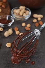 Photo of Whisk with chocolate cream and nuts on gray table, closeup