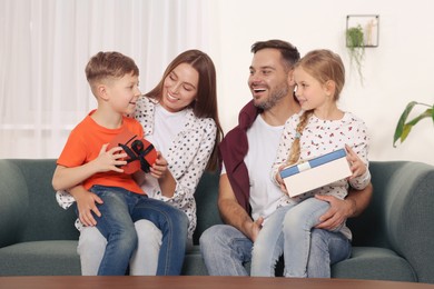 Photo of Happy family presenting each other with gifts on sofa at home