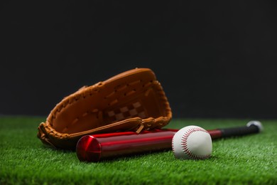 Baseball bat, leather glove and ball on green grass against dark background. Space for text