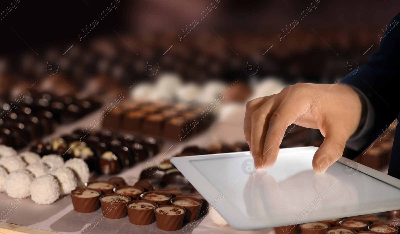 Image of Production line of chocolate candies. Man working with tablet, closeup