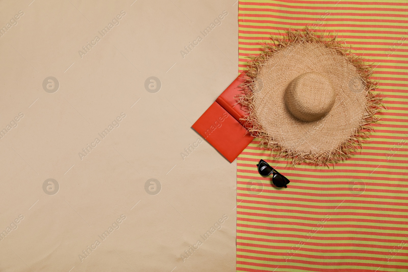 Photo of Striped beach towel, hat, open book and sunglasses on sand, top view. Space for text