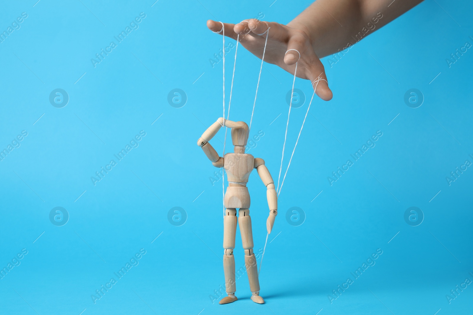 Photo of Woman pulling strings of puppet on light blue background, closeup