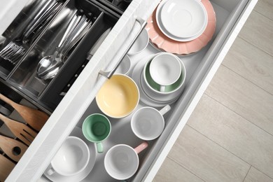 Photo of Ceramic dishware, utensils and cutlery in drawers, top view