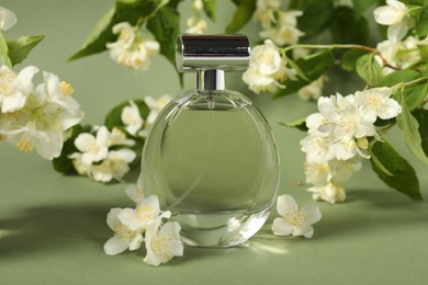 Photo of Aromatic perfume in bottle among beautiful jasmine flowers on pale green background