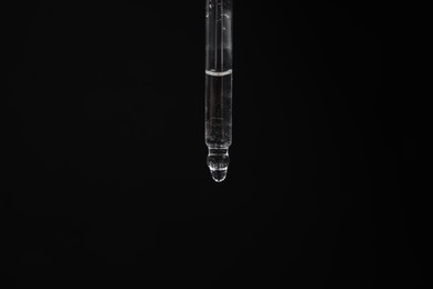 Photo of Dripping cosmetic serum from pipette against black background