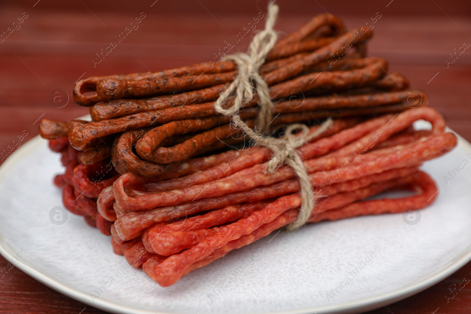 Photo of Bundles of delicious kabanosy on wooden table, closeup