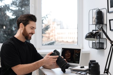 Professional photographer with digital camera at table in office, space for text