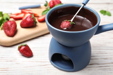 Fondue pot with chocolate and strawberries on white wooden table. Space for text