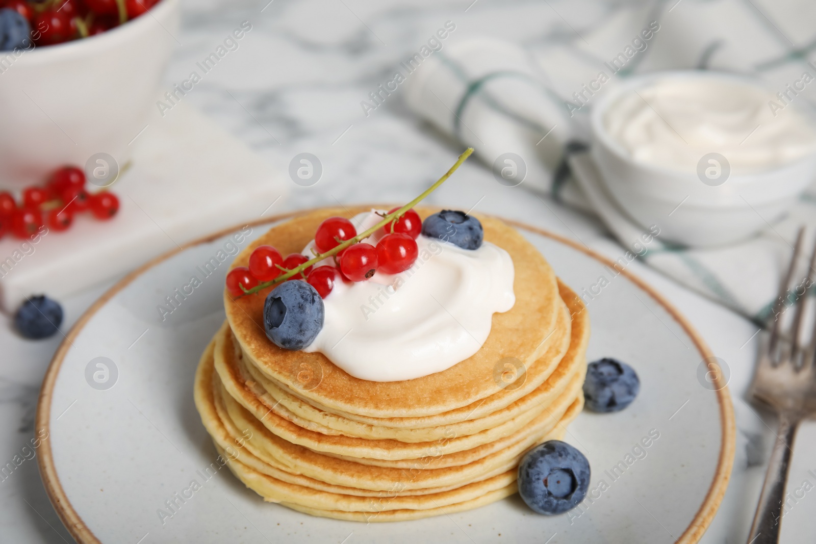 Photo of Tasty pancakes with natural yogurt, blueberries and red currants on marble table