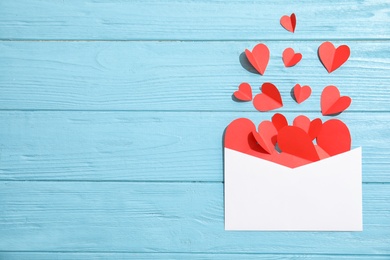 Photo of Envelope with small paper hearts on wooden background, top view