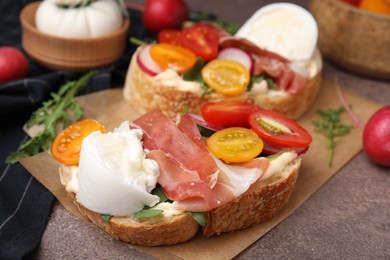 Photo of Delicious sandwiches with burrata cheese, ham, radish and tomatoes on brown textured table, closeup