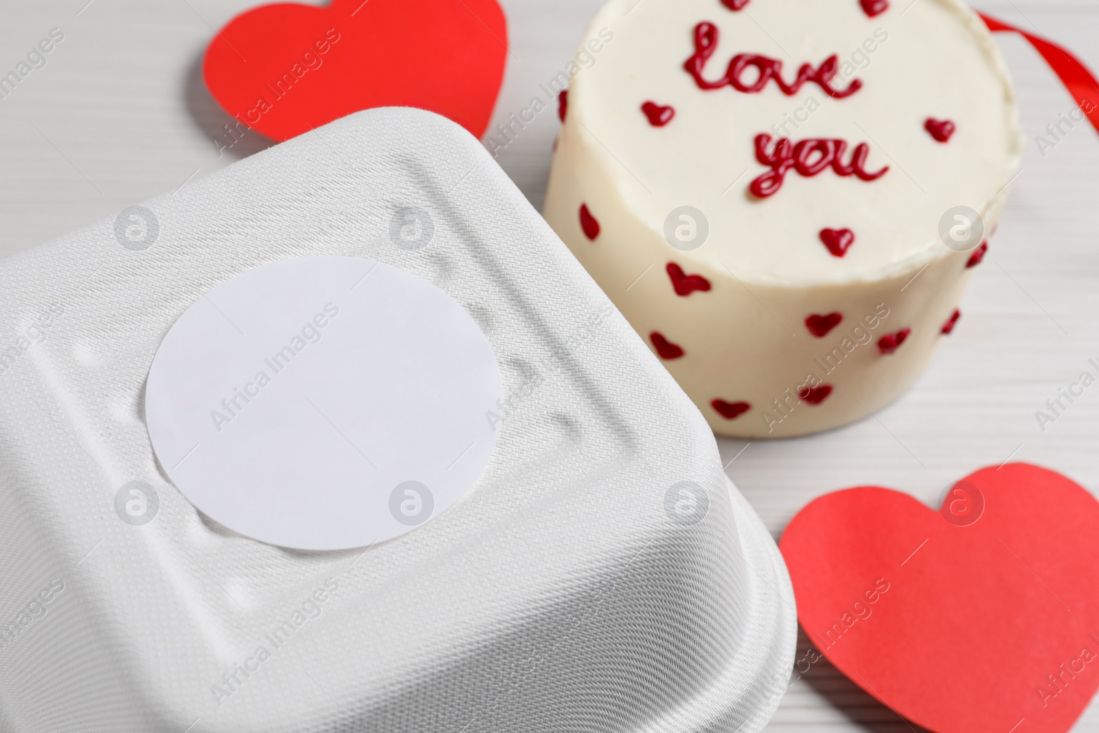 Photo of Bento cake with text Love You and takeaway packaging on white table