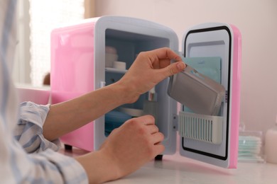 Photo of Woman taking cosmetic product from mini fridge indoors, closeup