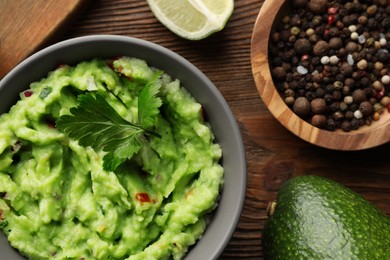 Photo of Delicious guacamole and ingredients on wooden table, flat lay