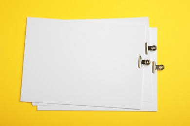 Photo of Sheets of paper with clips on yellow background, top view