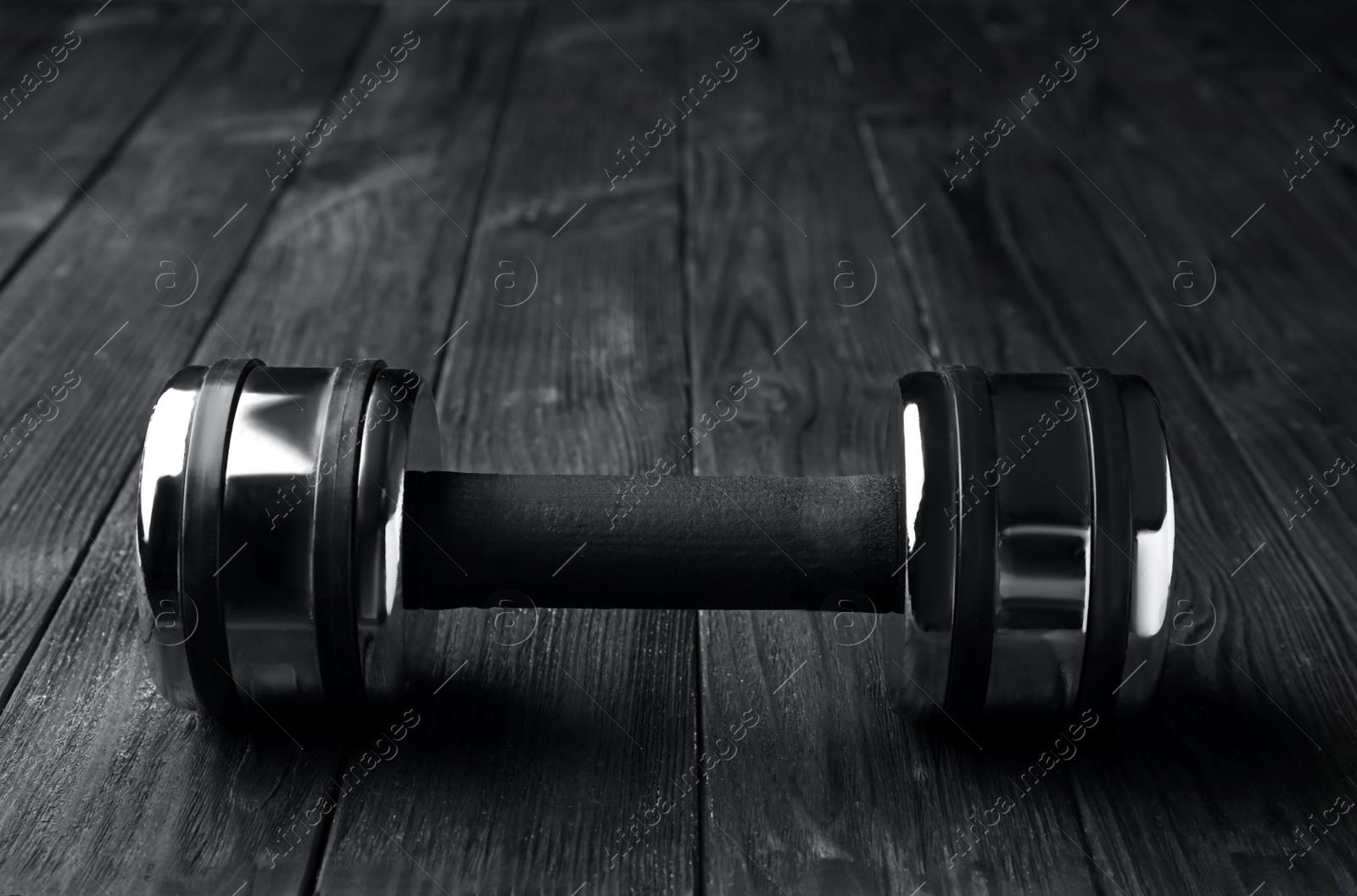 Photo of One metal dumbbell on black wooden table