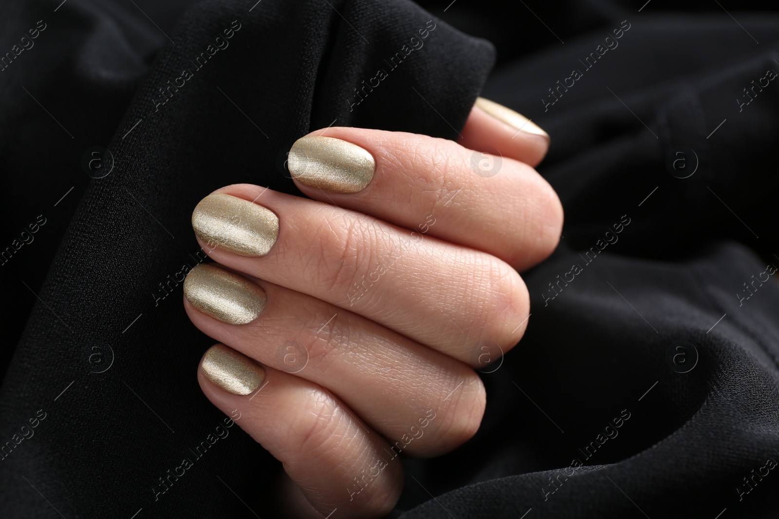 Photo of Woman with golden manicure holding black fabric, closeup. Nail polish trends