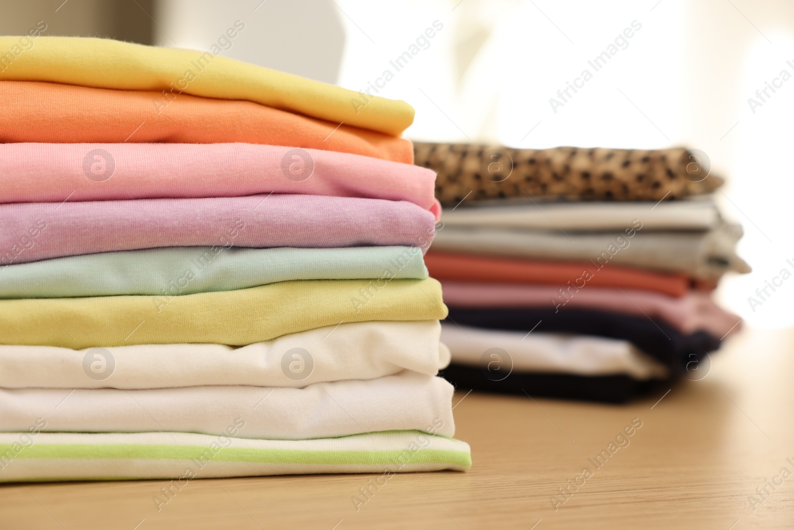 Photo of Many stacked clean clothes on wooden table, closeup