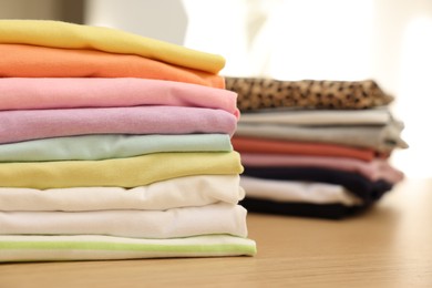 Photo of Many stacked clean clothes on wooden table, closeup