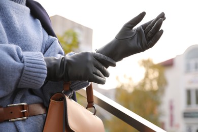 Photo of Young woman putting on stylish black leather gloves outdoors, closeup