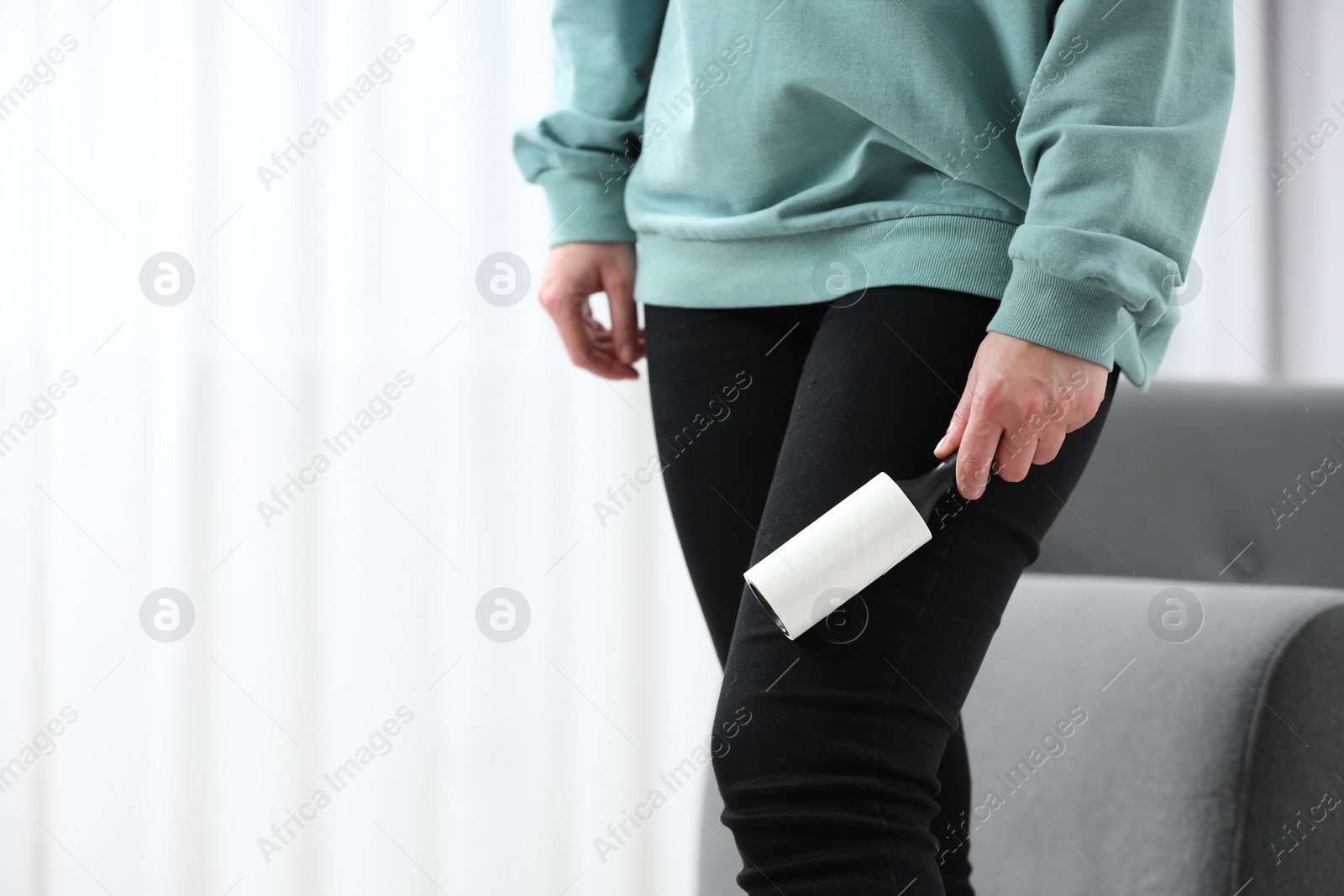 Photo of Woman with lint roller removing pet hair from black trousers indoors, closeup. Space for text