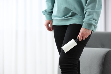 Woman with lint roller removing pet hair from black trousers indoors, closeup. Space for text