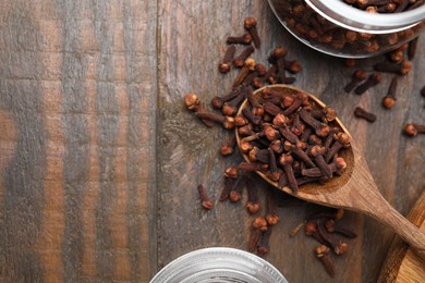 Photo of Glass jar and spoon with aromatic cloves on wooden table, flat lay. Space for text