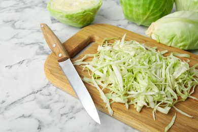 Photo of Chopped ripe cabbage and knife on white marble table, closeup