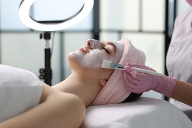 Photo of Cosmetologist applying mask on woman's face in clinic, closeup