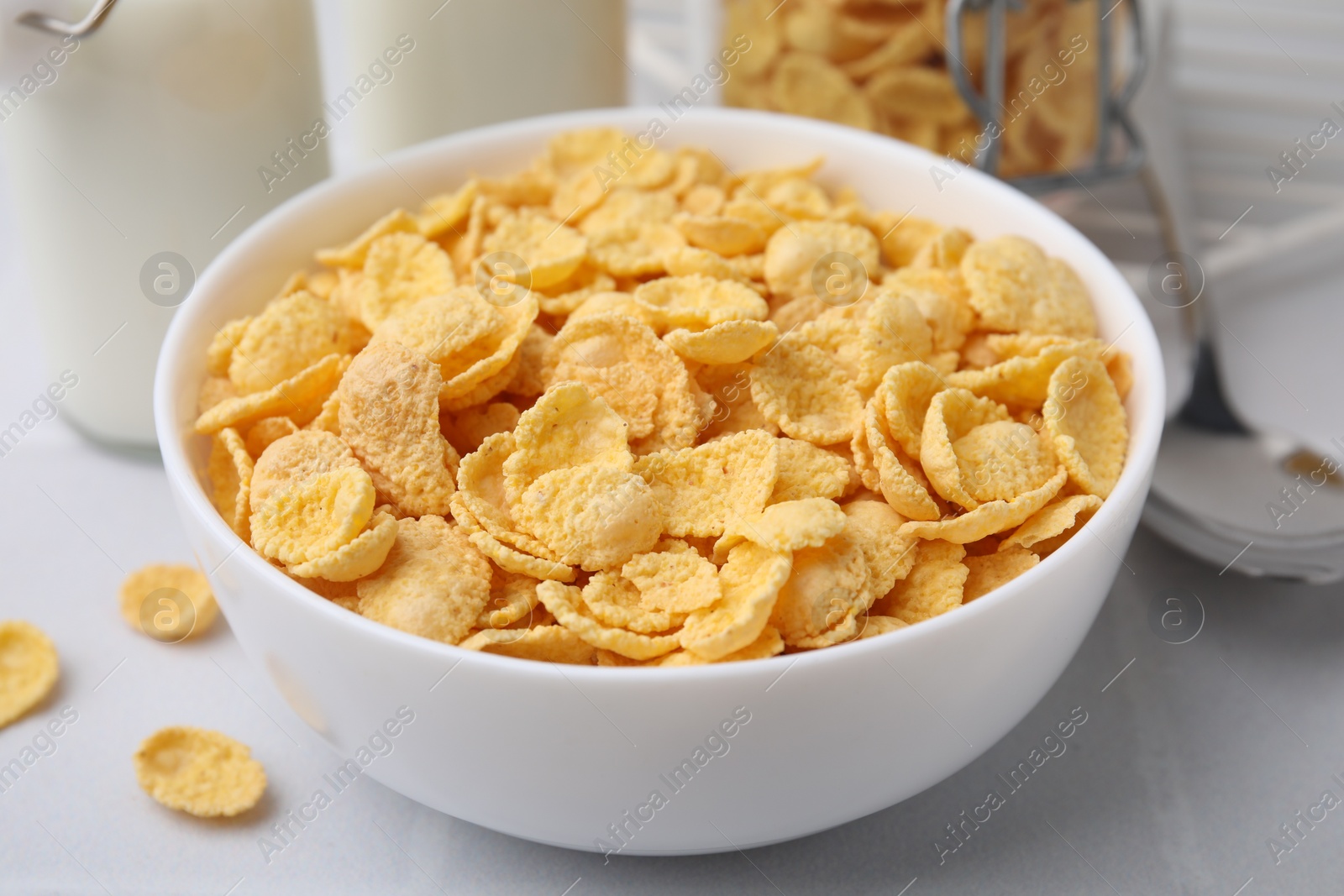 Photo of Tasty crispy corn flakes in bowl on white table, closeup. Breakfast cereal