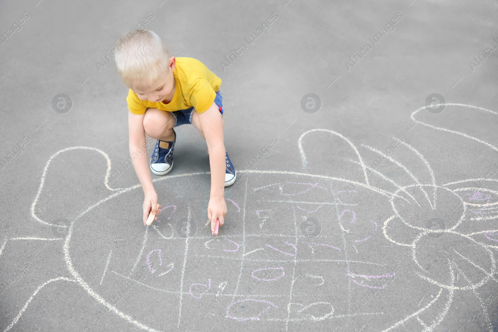 Photo of Little child drawing bunny with colorful chalk on asphalt