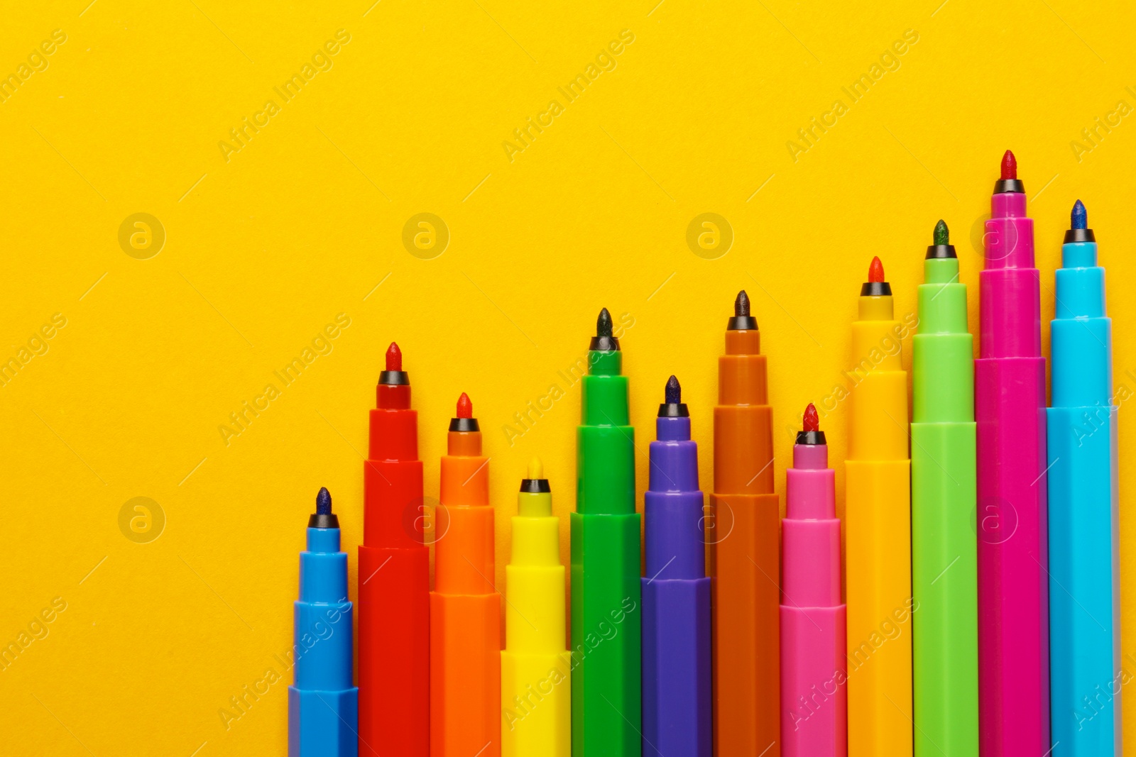 Photo of Many bright markers on yellow background, flat lay. Space for text