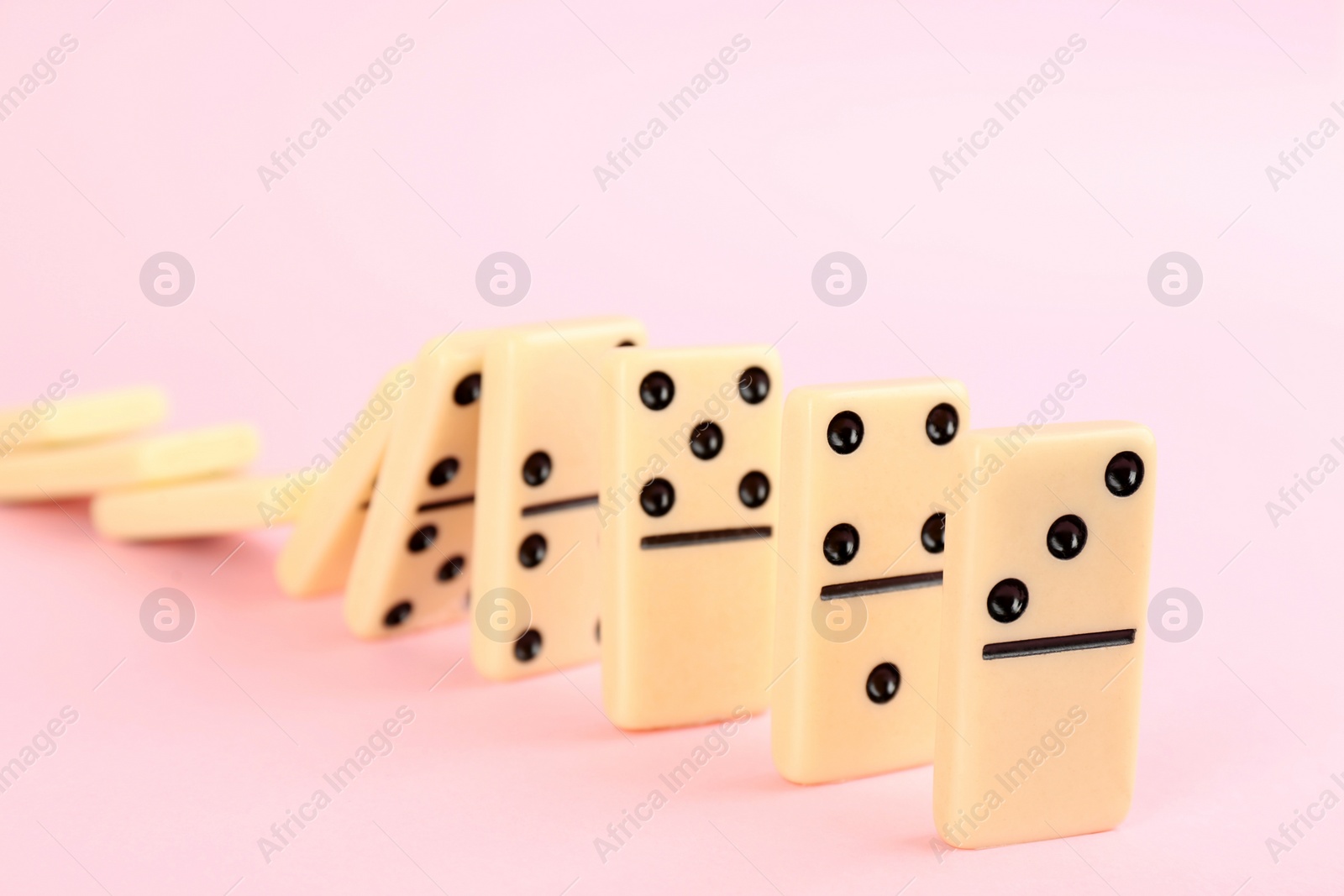 Photo of White domino tiles falling on pink background