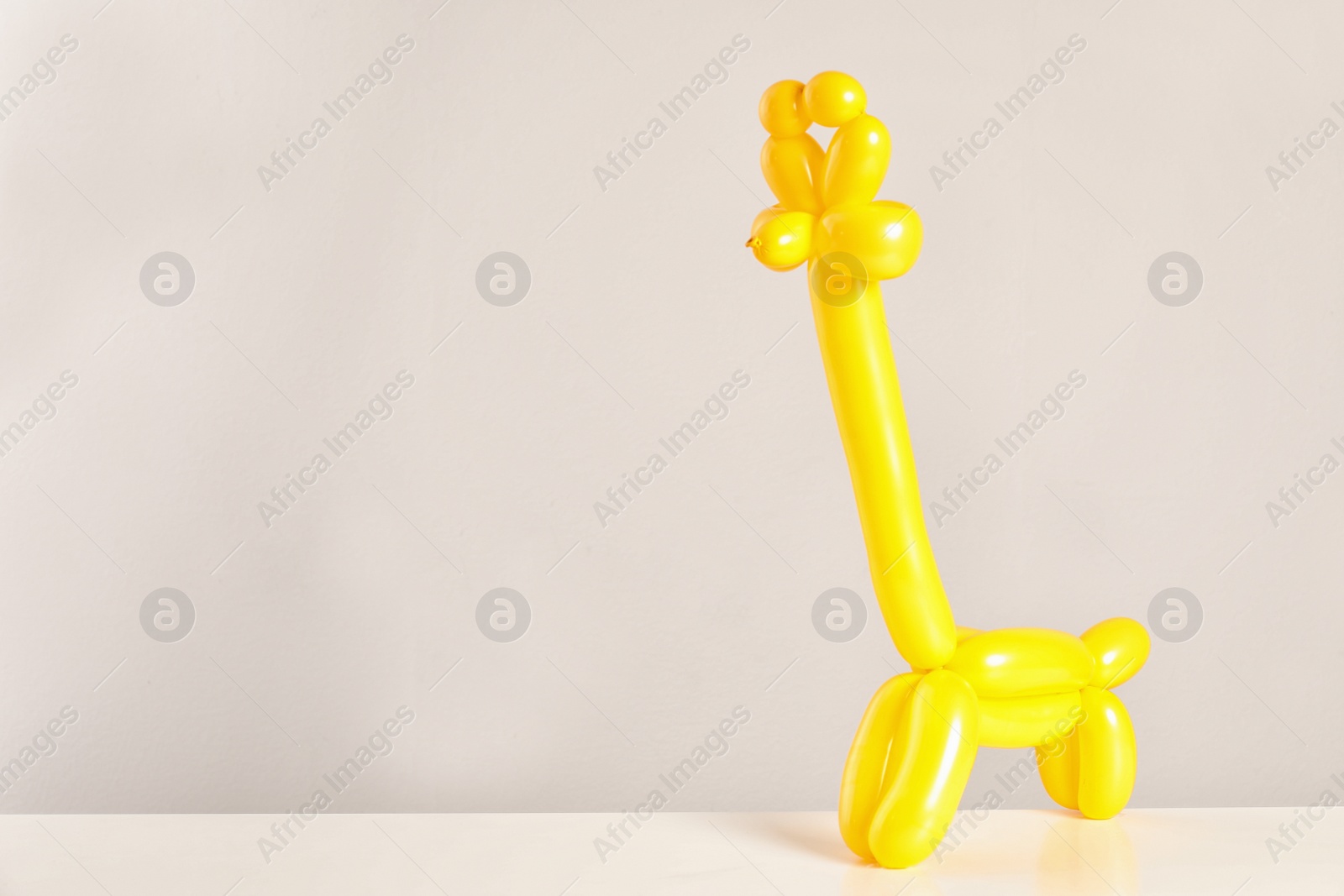 Photo of Giraffe figure made of modelling balloon on table against color background. Space for text