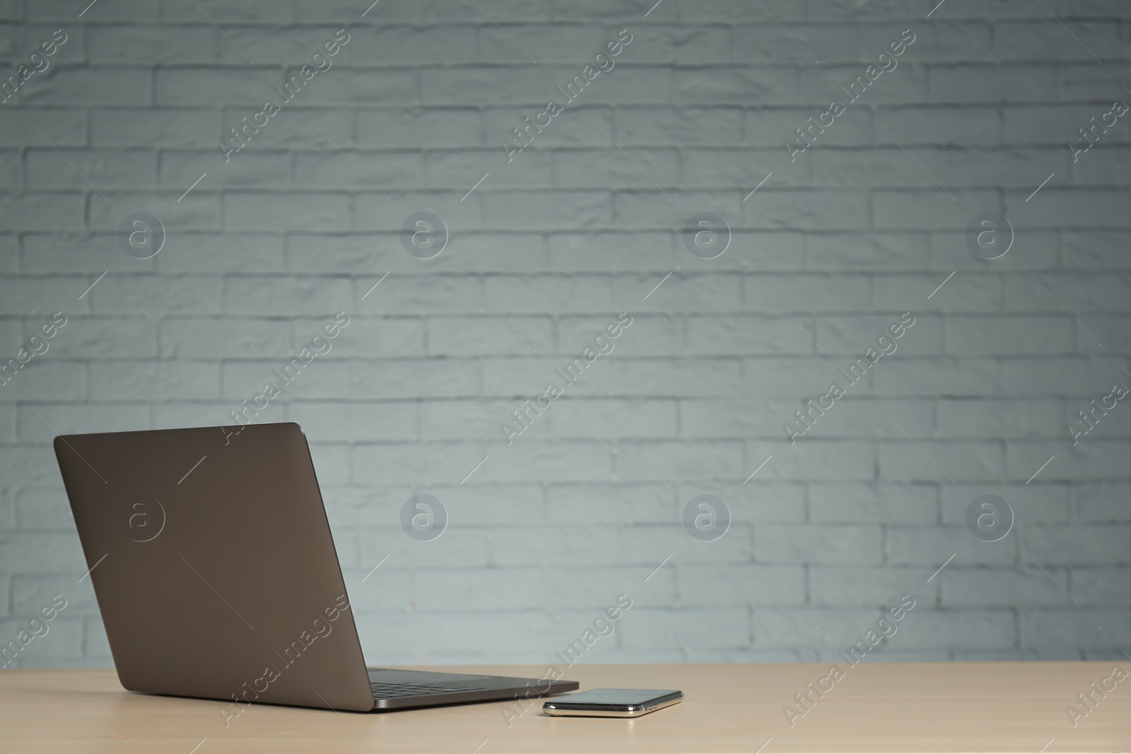 Photo of Modern laptop and mobile phone on table against brick wall