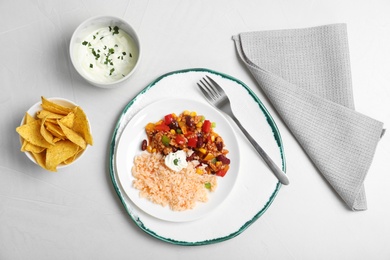 Photo of Chili con carne served with sauce and tortilla chips on light table, top view