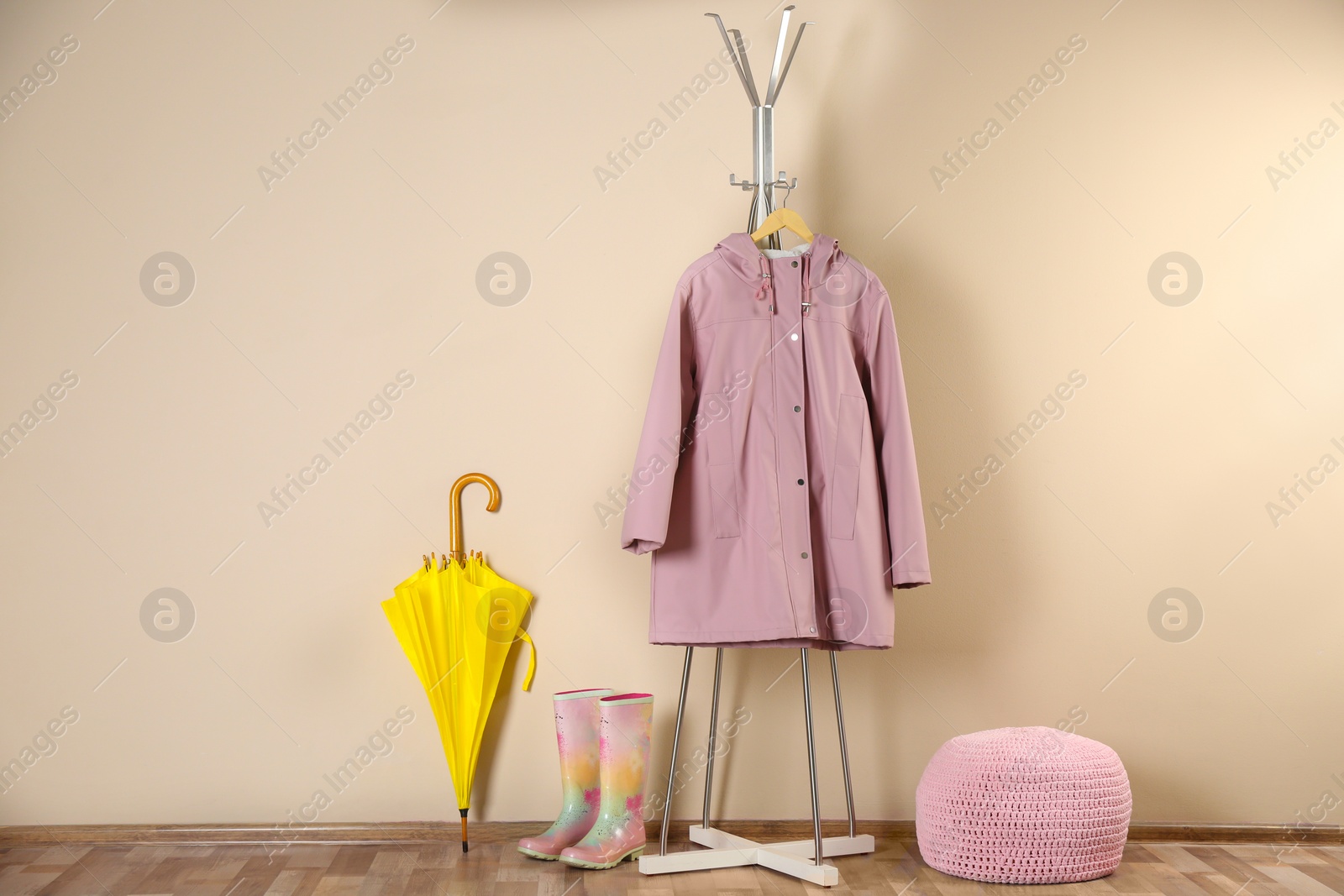 Photo of Yellow umbrella, raincoat and rubber boots near beige wall