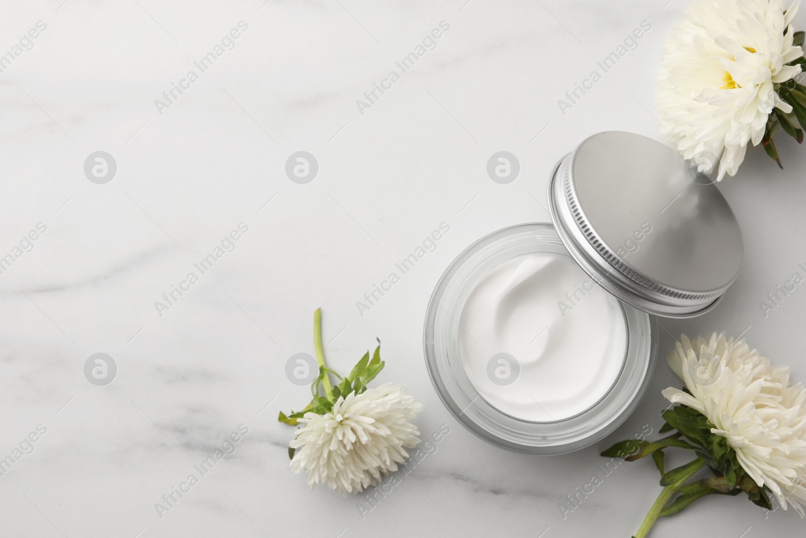 Photo of Glass jar of face cream and flowers on white marble table, flat lay. Space for text