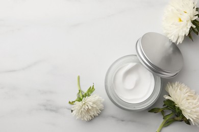 Glass jar of face cream and flowers on white marble table, flat lay. Space for text