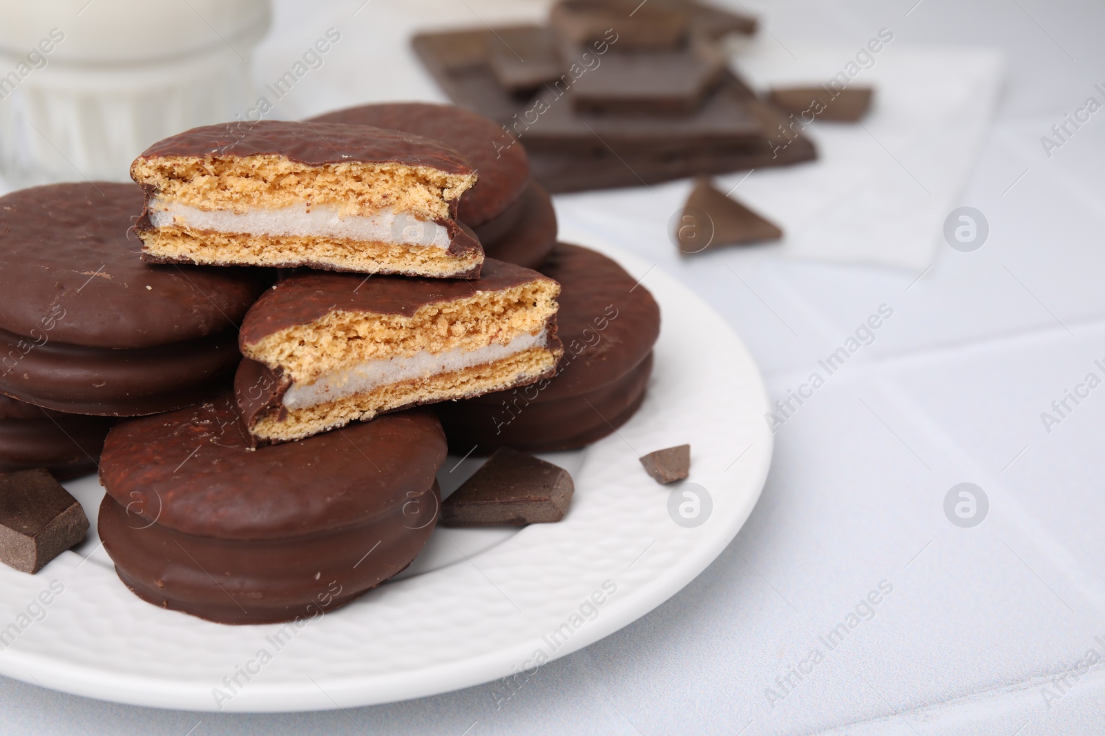 Photo of Tasty choco pies and pieces of chocolate on white tiled table, closeup. Space for text