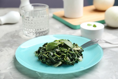 Photo of Tasty cooked spinach and fork on grey table. Healthy food